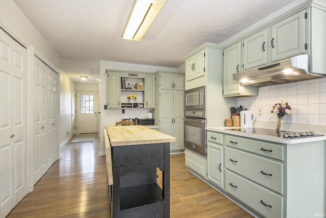 kitchen with oven, under cabinet range hood, butcher block counters, open shelves, and stainless steel microwave