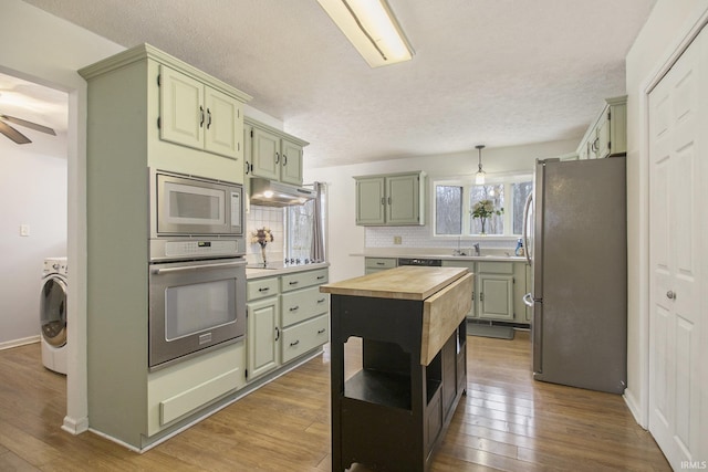 kitchen featuring stainless steel appliances, butcher block counters, wood-type flooring, washer / dryer, and under cabinet range hood