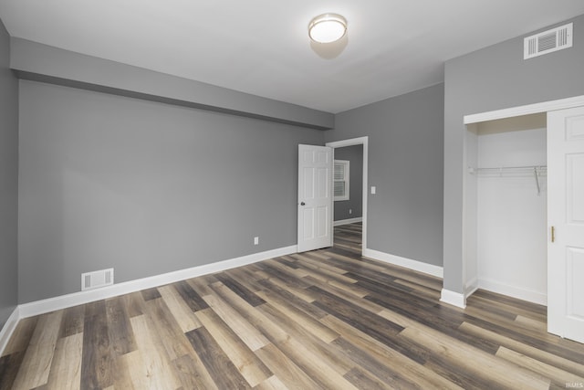 unfurnished bedroom with a closet, visible vents, baseboards, and wood finished floors