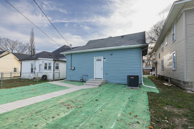 back of property featuring a shingled roof, a lawn, entry steps, central AC, and fence