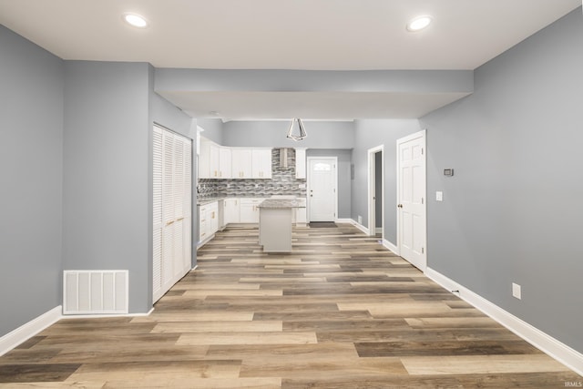 kitchen with wall chimney exhaust hood, visible vents, backsplash, white cabinets, and baseboards