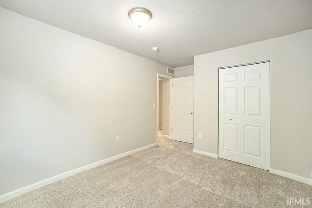 unfurnished bedroom featuring light carpet, visible vents, baseboards, and a closet