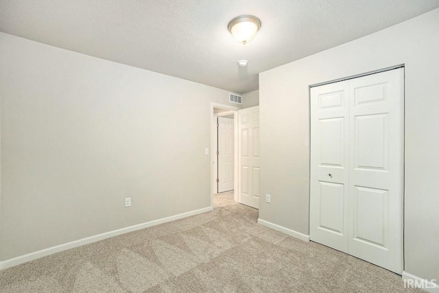 unfurnished bedroom with baseboards, visible vents, a textured ceiling, carpet floors, and a closet