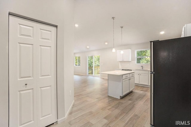 kitchen featuring light wood finished floors, white cabinets, a kitchen island, freestanding refrigerator, and backsplash