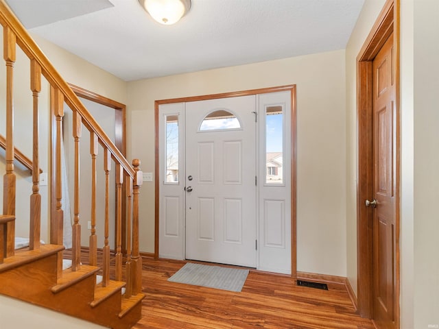 entryway with stairway, wood finished floors, visible vents, and baseboards