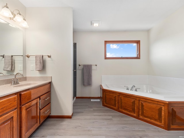 bathroom with a shower with door, vanity, wood finished floors, baseboards, and a bath