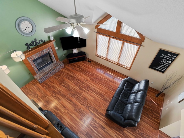 living area featuring visible vents, a ceiling fan, a brick fireplace, vaulted ceiling, and wood finished floors