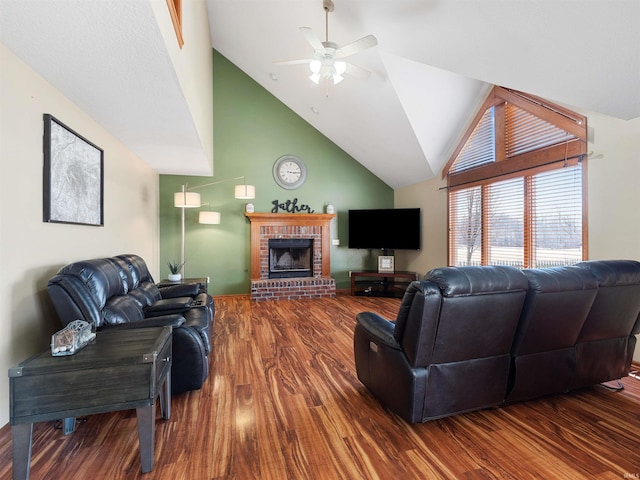 living area with high vaulted ceiling, a brick fireplace, a ceiling fan, and wood finished floors