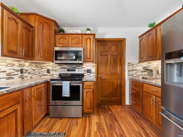 kitchen featuring tasteful backsplash, appliances with stainless steel finishes, light stone counters, and dark wood-style flooring