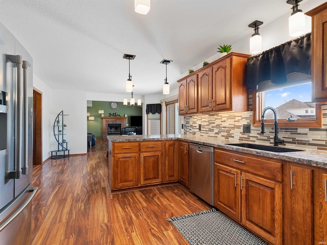 kitchen with brown cabinetry, dark wood-style floors, appliances with stainless steel finishes, a peninsula, and a sink