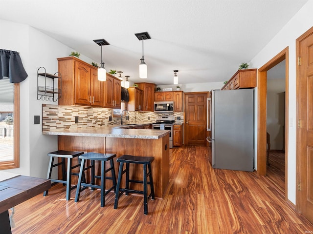 kitchen with appliances with stainless steel finishes, brown cabinetry, a sink, and a peninsula