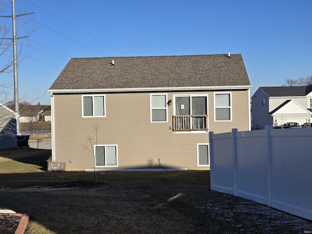 back of property with fence, a lawn, and roof with shingles