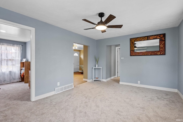 carpeted empty room with baseboards, visible vents, and a ceiling fan