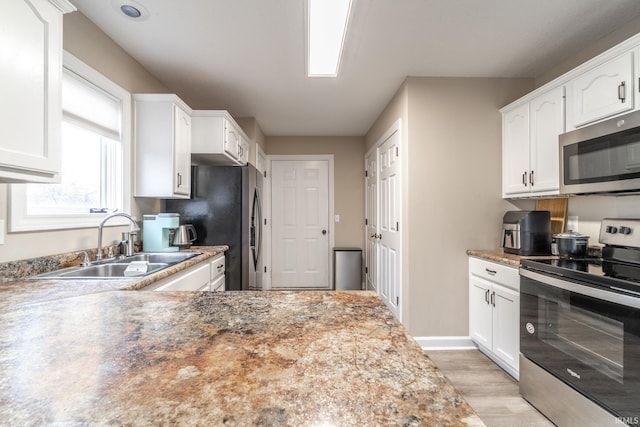 kitchen with light wood finished floors, baseboards, white cabinets, appliances with stainless steel finishes, and a sink