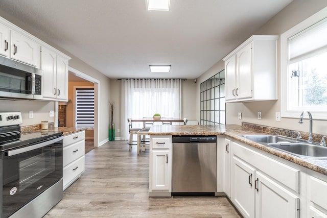 kitchen with appliances with stainless steel finishes, a wealth of natural light, white cabinets, and a sink