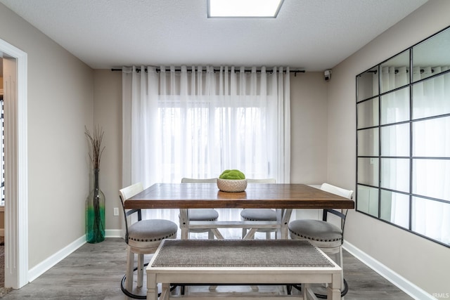 dining area with a textured ceiling, baseboards, and wood finished floors