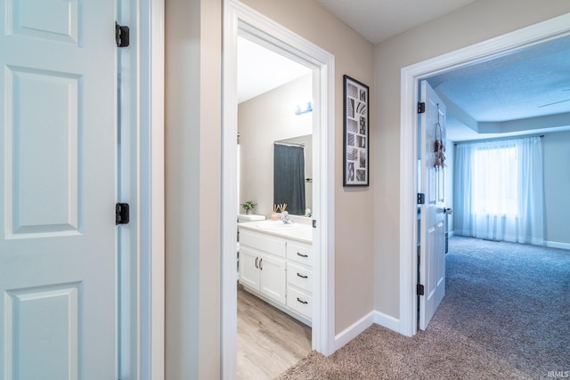 corridor featuring light carpet, a sink, and baseboards