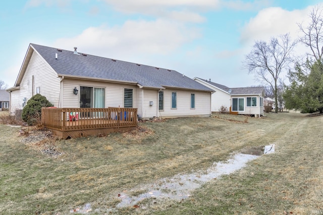 back of property with a shingled roof, a deck, and a lawn