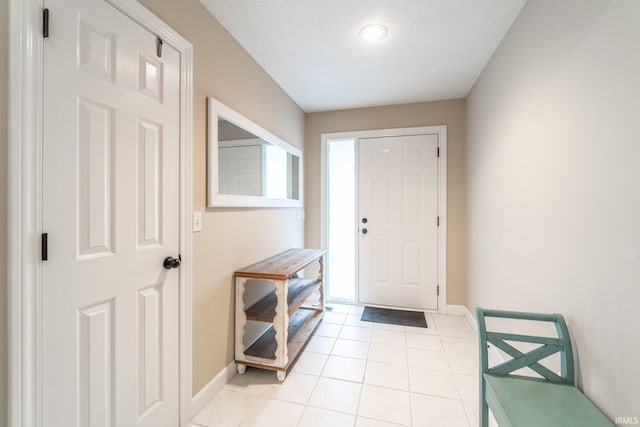 doorway featuring light tile patterned floors, a textured ceiling, and baseboards