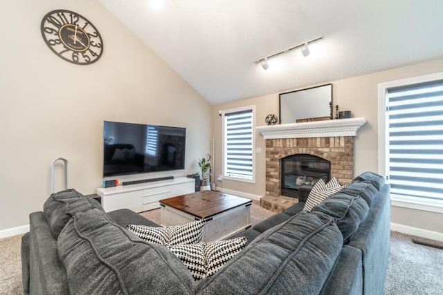 carpeted living area with vaulted ceiling, a brick fireplace, rail lighting, and baseboards