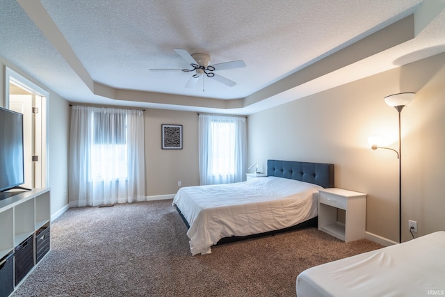 carpeted bedroom featuring a ceiling fan, a tray ceiling, baseboards, and a textured ceiling