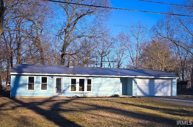 single story home featuring a chimney, an attached garage, metal roof, driveway, and a front lawn