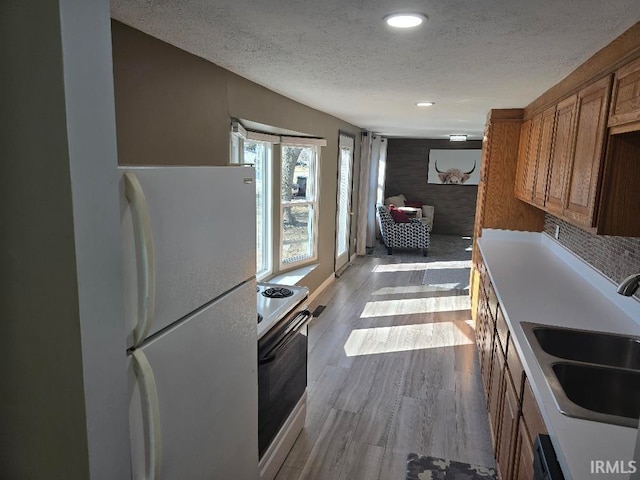 kitchen with brown cabinets, light wood-style floors, a sink, a textured ceiling, and white appliances