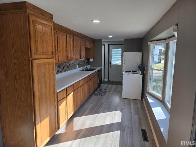 kitchen with light countertops, decorative backsplash, a sink, wood finished floors, and white appliances