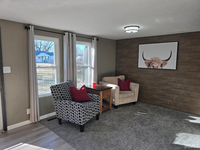 sitting room featuring an accent wall, wood walls, wood finished floors, and baseboards