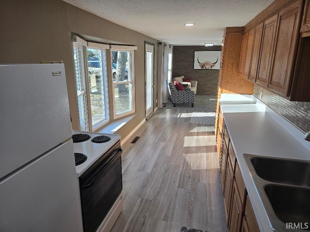 kitchen featuring brown cabinets, electric range oven, freestanding refrigerator, a sink, and wood finished floors