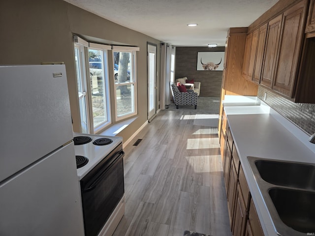 kitchen featuring visible vents, freestanding refrigerator, light wood-type flooring, a sink, and range with electric stovetop