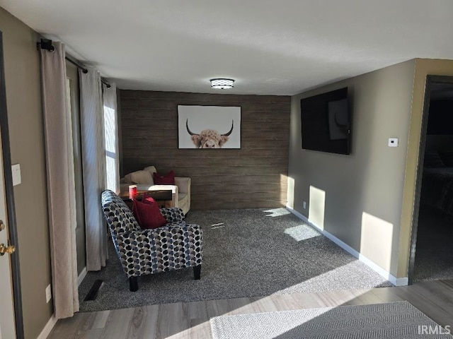 sitting room featuring an accent wall, wood walls, baseboards, and wood finished floors