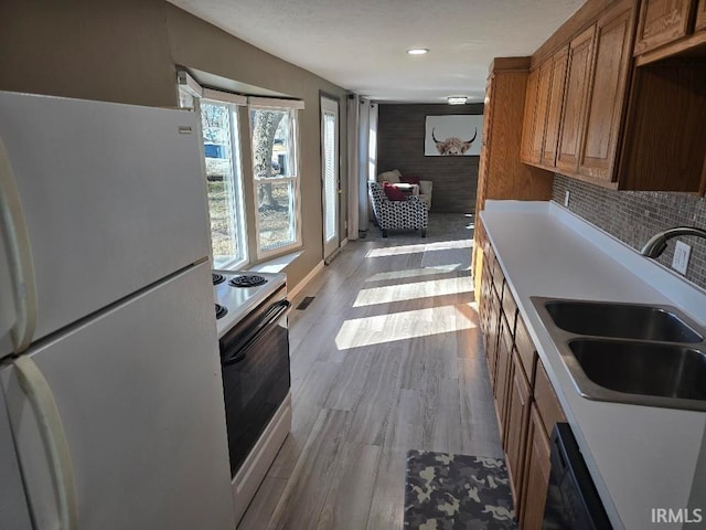 kitchen with brown cabinets, range with electric stovetop, freestanding refrigerator, a sink, and wood finished floors