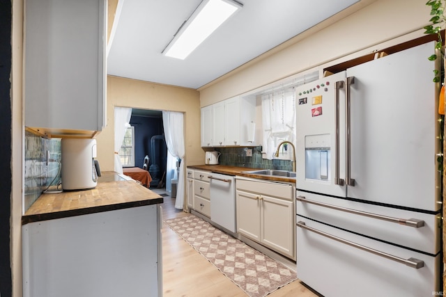 kitchen featuring white appliances, tasteful backsplash, light wood finished floors, white cabinets, and a sink