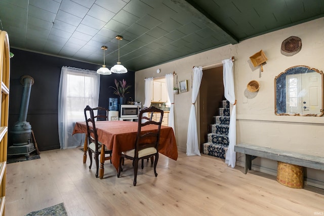 dining area featuring stairs, ornamental molding, light wood-type flooring, and a wood stove