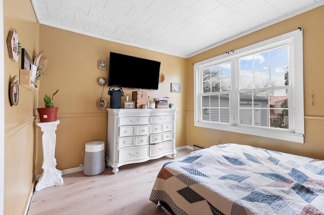 bedroom featuring baseboard heating, wood finished floors, and wainscoting