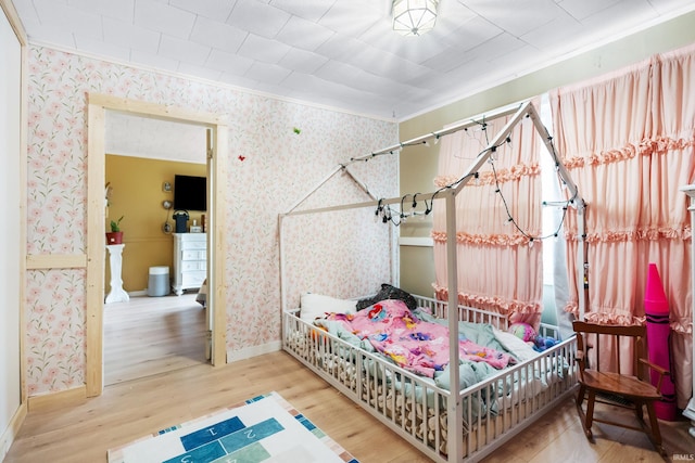 bedroom featuring baseboards, ornamental molding, wood finished floors, and wallpapered walls