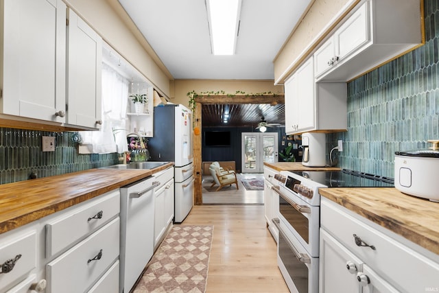 kitchen featuring decorative backsplash, white cabinetry, a sink, wood counters, and white appliances