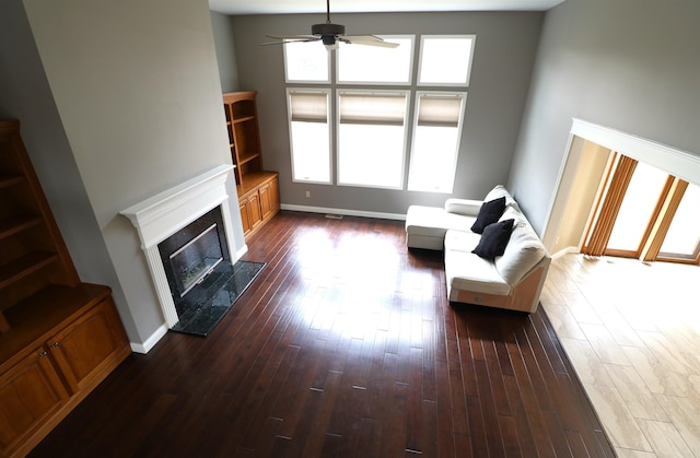 unfurnished living room with ceiling fan, dark wood finished floors, a high end fireplace, and baseboards