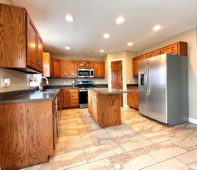 kitchen featuring dark countertops, appliances with stainless steel finishes, brown cabinets, a center island, and a sink