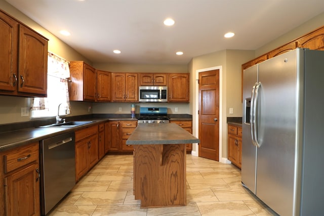 kitchen with dark countertops, a kitchen island, appliances with stainless steel finishes, brown cabinets, and a sink