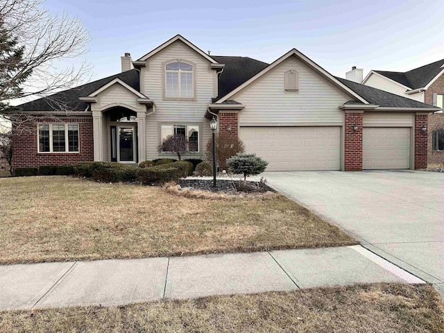 traditional-style house featuring brick siding, a chimney, concrete driveway, an attached garage, and a front lawn