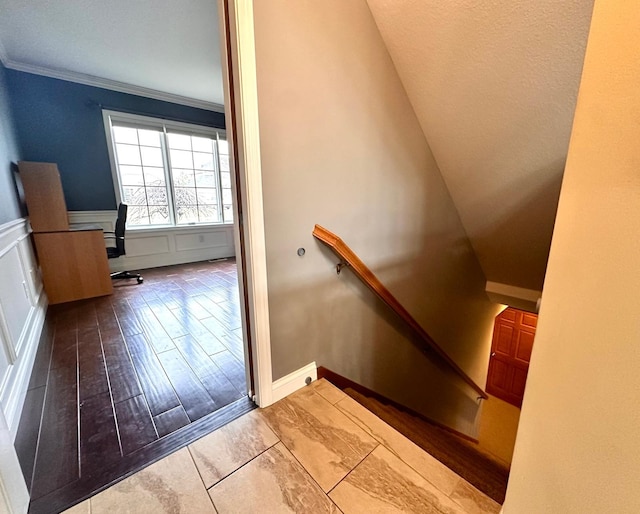 stairway featuring ornamental molding, a decorative wall, wood finished floors, and wainscoting