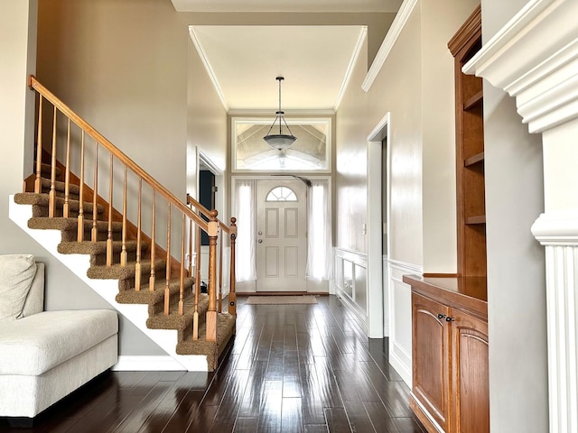 foyer featuring stairway, dark wood-type flooring, crown molding, and a decorative wall