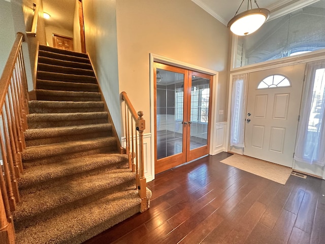 entryway with french doors, a decorative wall, a towering ceiling, ornamental molding, and dark wood-type flooring