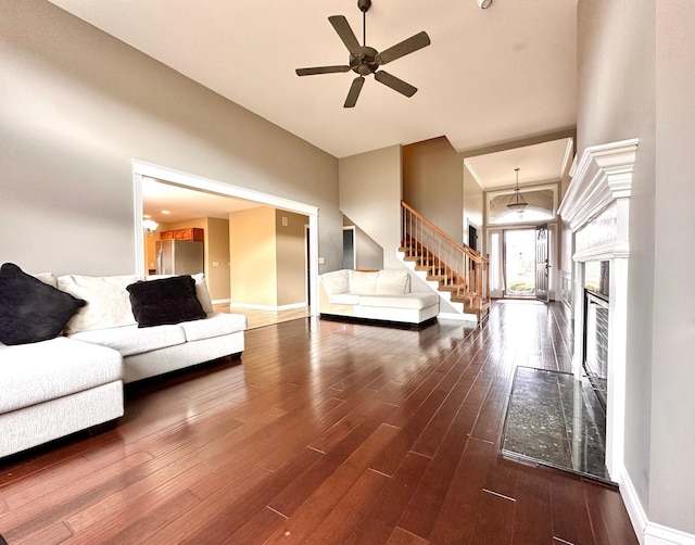 unfurnished living room featuring dark wood-style floors, ceiling fan, stairway, and baseboards