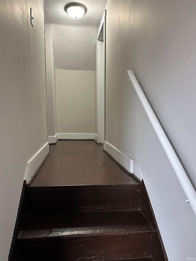 staircase with a textured ceiling, wood finished floors, lofted ceiling, and baseboards