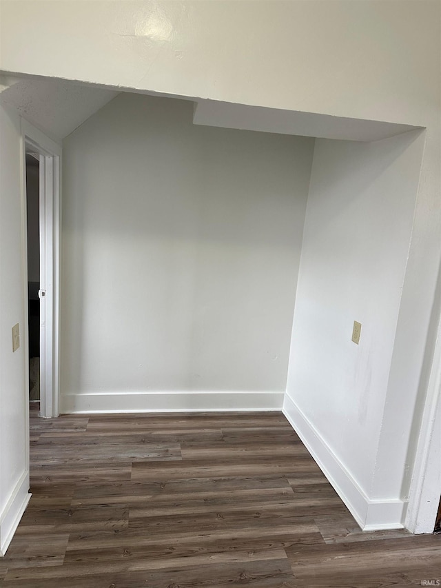 spare room with dark wood-style flooring, vaulted ceiling, and baseboards