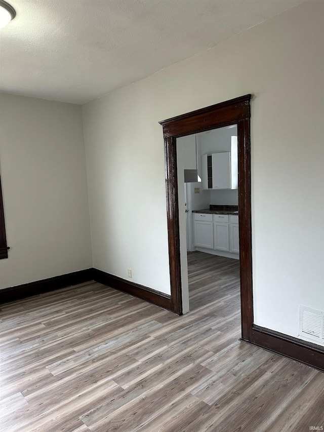 spare room with baseboards, visible vents, a textured ceiling, and light wood finished floors