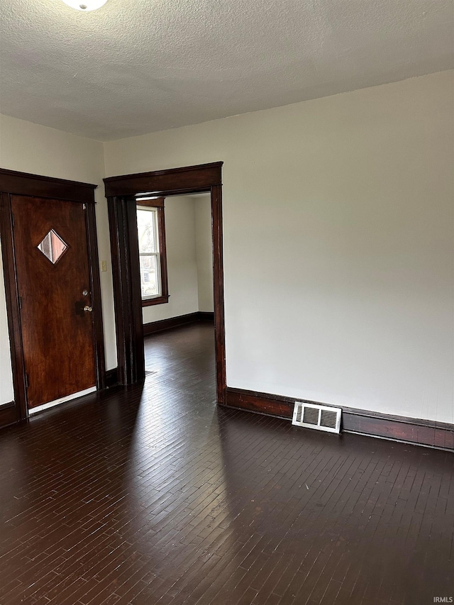 empty room with a textured ceiling, hardwood / wood-style flooring, visible vents, and baseboards